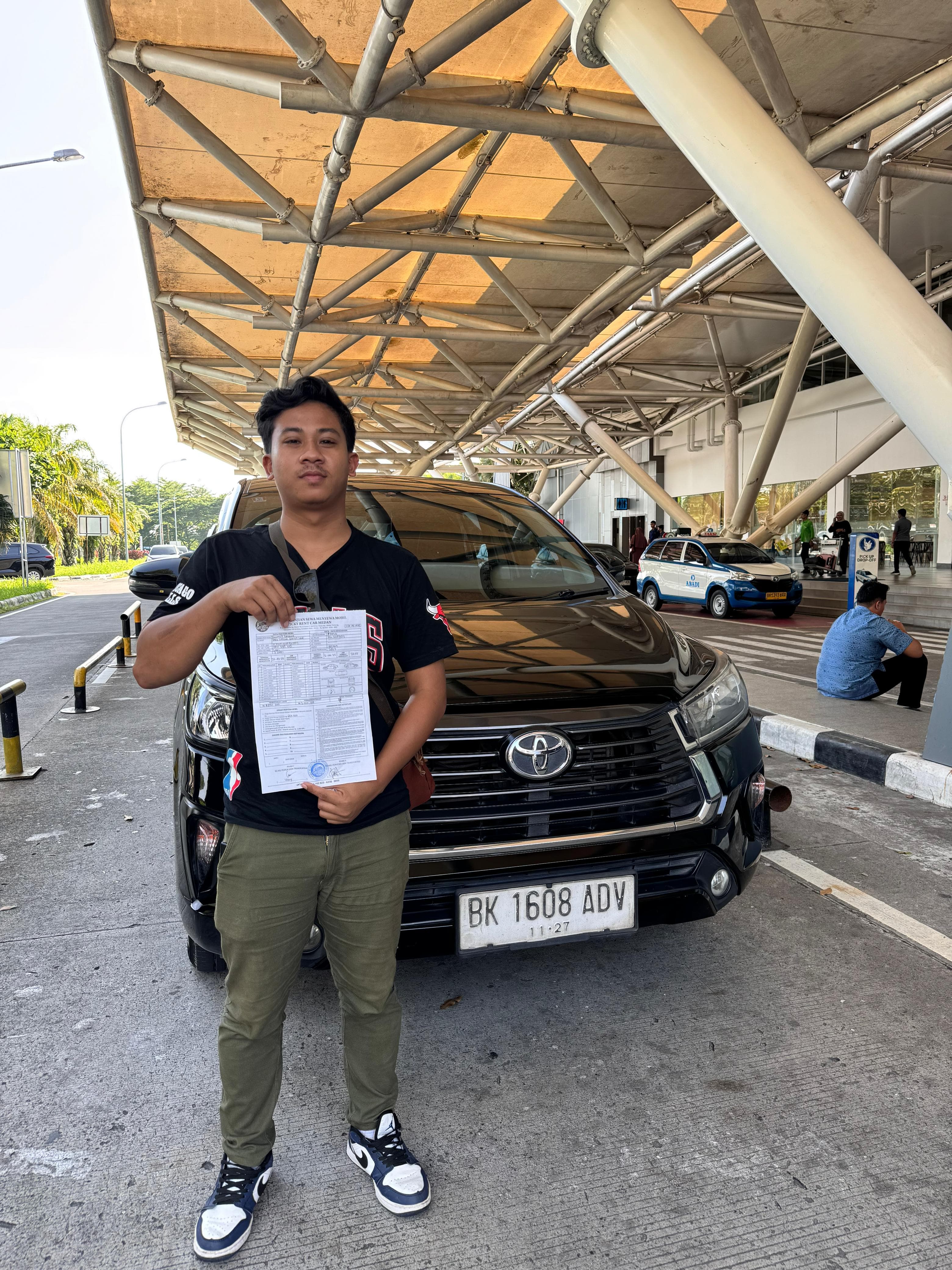 Foto pelanggan berpose di depan mobil sewaan